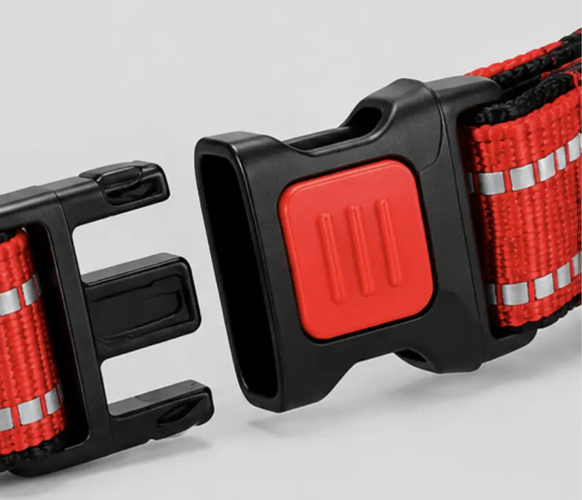 Close-up of a red and black safety belt buckle with reflective silver stripes on a light gray background.