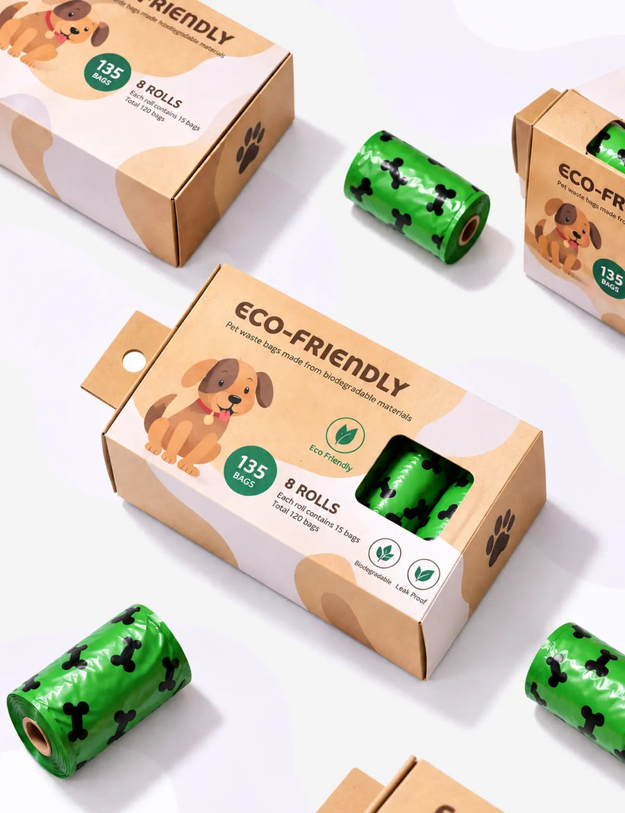 Eco-friendly dog poop bags shown with their kraft paper packaging boxes and several rolls of green bags printed with black poop-shaped silhouettes, arranged on a clean white background.